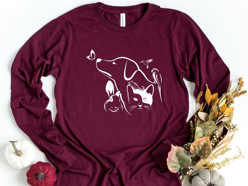 Op de afbeelding: Een bordeauxrood T-shirt met lange mouwen met een wit silhouetontwerp van een hond, een kat, een konijn, een vlinder en een vogel.
