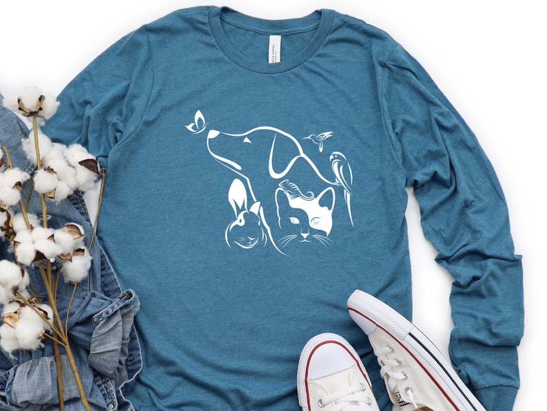 Op de afbeelding: Een tealblauw longsleeve t-shirt met een witte afbeelding van een hond, een kat, een konijn en twee vogels. De afbeelding is gecentreerd op het shirt.