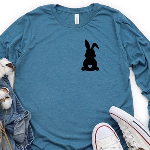 May include: A teal blue long-sleeved shirt with a black silhouette of a bunny rabbit with a heart on its chest.