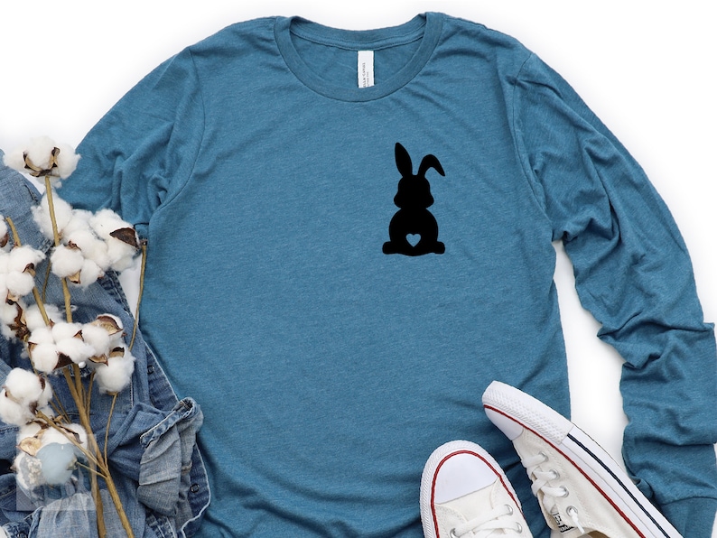 May include: A teal blue long-sleeved shirt with a black silhouette of a bunny rabbit with a heart on its chest.