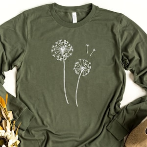 May include: A long-sleeved, olive green t-shirt featuring a white graphic of two dandelions. The dandelions are stylised and have a simple, minimalist design.