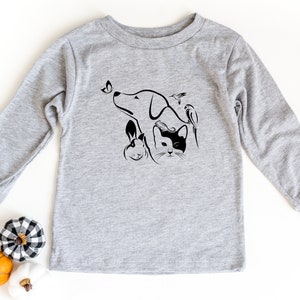 Op de afbeelding: Een grijs longsleeve shirt met een zwart-witte afbeelding van een hond, kat, konijn en vogel. De afbeelding is gestileerd en heeft een vlinder.