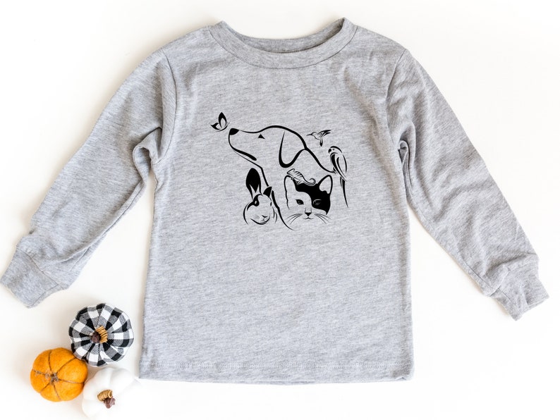 Op de afbeelding: Een grijs longsleeve shirt met een zwart-witte afbeelding van een hond, kat, konijn en vogel. De afbeelding is gestileerd en heeft een vlinder.