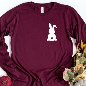 May include: A maroon long-sleeved t-shirt with a white silhouette of a bunny rabbit with a heart on its chest.