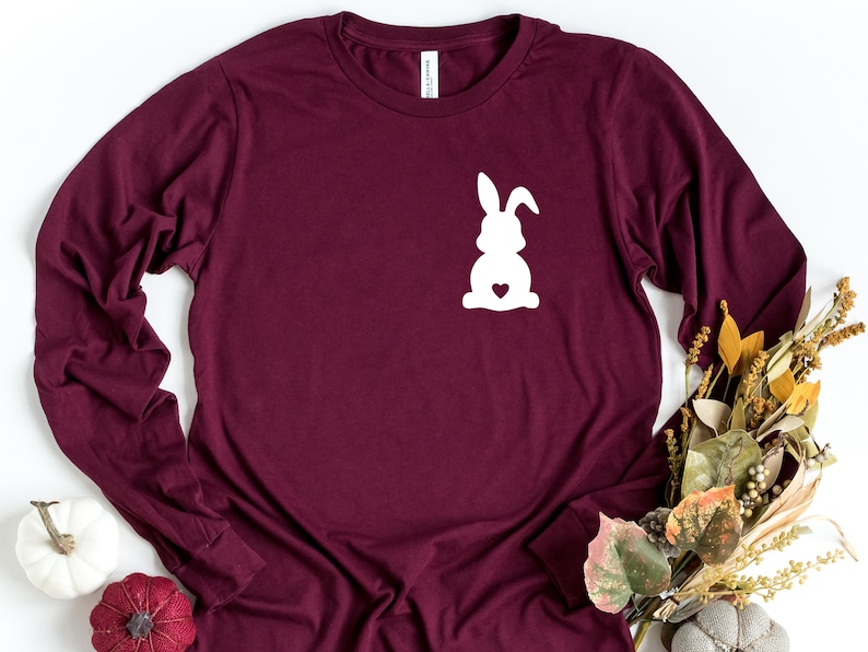 May include: A maroon long-sleeved t-shirt with a white silhouette of a bunny rabbit with a heart on its chest.