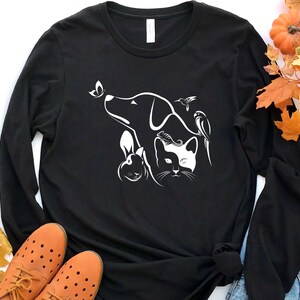 Op de afbeelding: Zwart longsleeve t-shirt met een wit grafisch ontwerp van een hond, een kat, een konijn, een vlinder en een vogel. Het ontwerp is gecentreerd op het shirt.