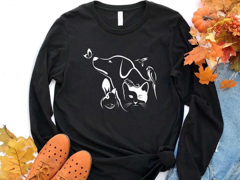 Op de afbeelding: Zwart longsleeve t-shirt met een wit grafisch ontwerp van een hond, een kat, een konijn, een vlinder en een vogel. Het ontwerp is gecentreerd op het shirt.