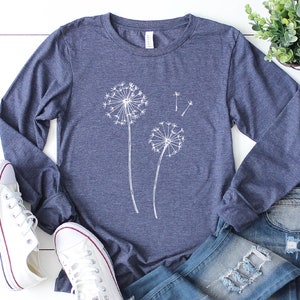May include: A navy blue long-sleeved t-shirt with a white dandelion graphic. The shirt is made of a soft, comfortable material.