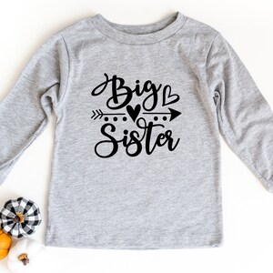 May include: Gray long-sleeve shirt with black text that reads "Big Sister" with an arrow and hearts.