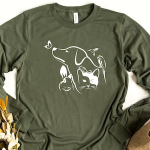Op de afbeelding: Een groen longsleeve t-shirt met een wit grafisch ontwerp van een hond, kat, konijn, vlinder en kolibrie.