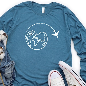 May include: A teal blue long-sleeved t-shirt with a white outline of the world and a plane flying above it.