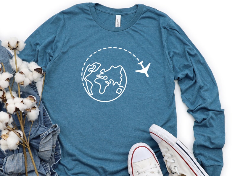 May include: A teal blue long-sleeved t-shirt with a white outline of the world and a plane flying above it.