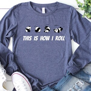 May include: A navy blue long-sleeved t-shirt with a graphic of five pandas rolling down a hill. The text "This is how I roll" is printed below the pandas.