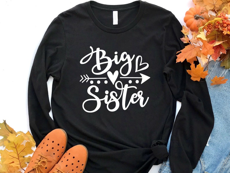 May include: Black long-sleeve shirt with white text that reads "Big Sister" with an arrow and hearts.