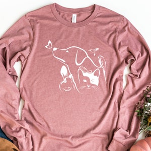 Op de afbeelding: Een langarm, mauve t-shirt met een wit grafisch ontwerp van een hond, een kat, een konijn en twee vogels. Het ontwerp is gecentreerd op het shirt.