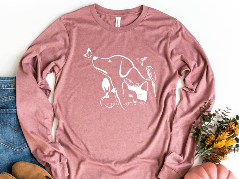 Op de afbeelding: Een langarm, mauve t-shirt met een wit grafisch ontwerp van een hond, een kat, een konijn en twee vogels. Het ontwerp is gecentreerd op het shirt.