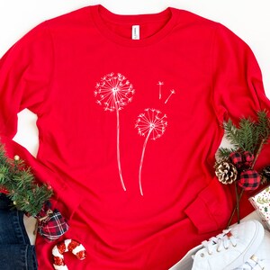 May include: Red long-sleeved t-shirt with a white dandelion design.