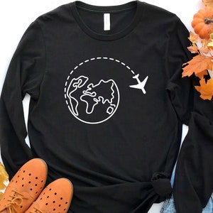 May include: Black long-sleeve t-shirt with a white outline of a globe and airplane, representing travel.
