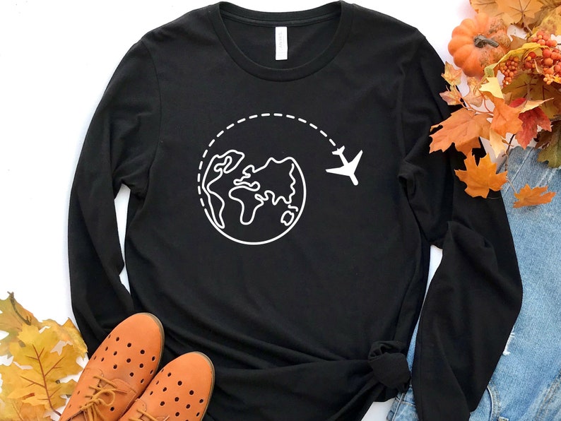 May include: Black long-sleeve t-shirt with a white outline of a globe and airplane, representing travel.