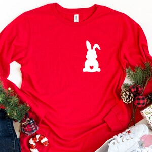May include: Red long-sleeved shirt with a white silhouette of a bunny rabbit with a heart in its chest.