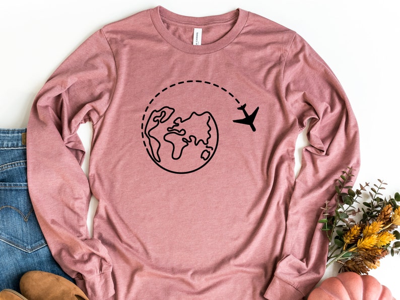 May include: A long-sleeved t-shirt in a dusty rose color with a black graphic of a plane flying around the world.