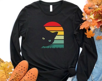 May include: Black long-sleeve t-shirt with a retro sunset graphic and a black cat silhouette peeking out from behind it.