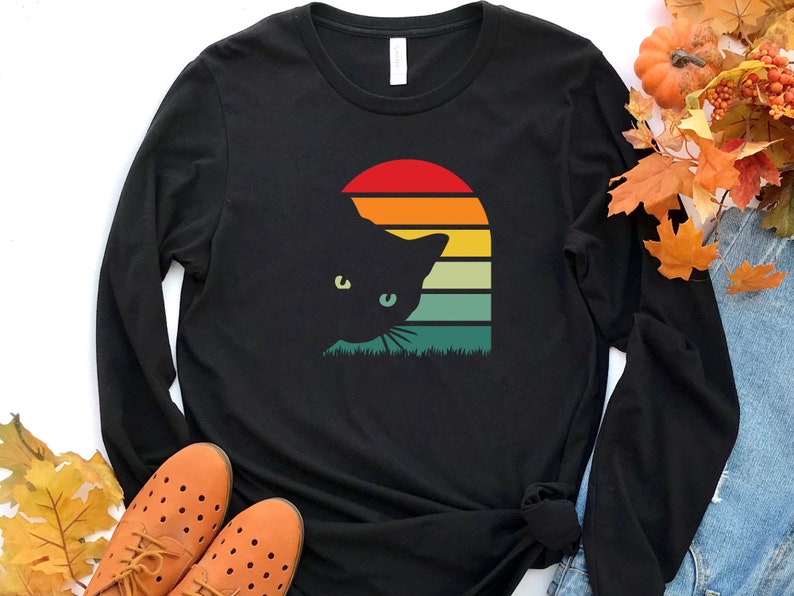 May include: Black long-sleeve t-shirt with a retro sunset graphic and a black cat silhouette peeking out from behind it.