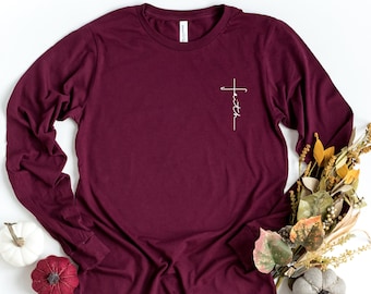 May include: Burgundy long-sleeve t-shirt with a white cross and the word "faith" printed on the left chest.