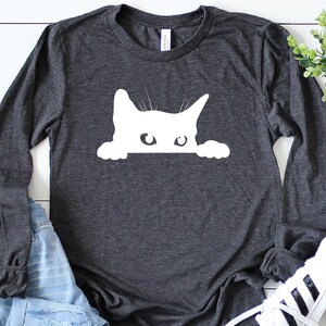 May include: A dark grey long-sleeved t-shirt with a white silhouette of a cat peeking over the top of the shirt.