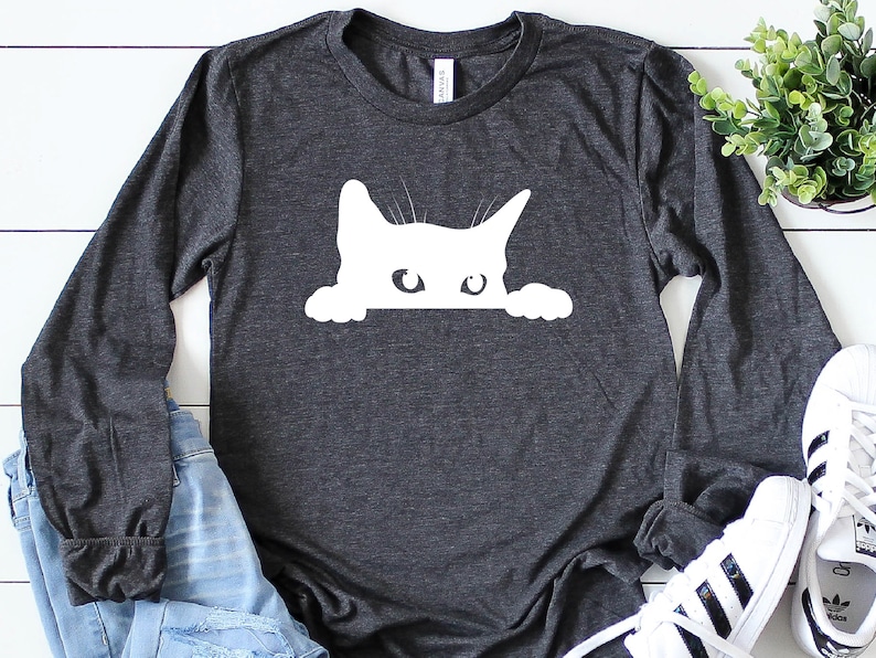 May include: A dark grey long-sleeved t-shirt with a white silhouette of a cat peeking over the top of the shirt.