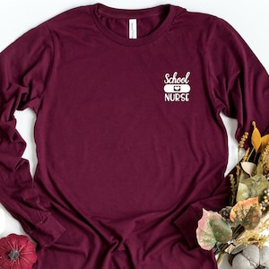 May include: Burgundy long-sleeve t-shirt with the text "School Nurse" and a white bandage with a heart on it.