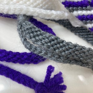 May include: Close-up of three strands of yarn in white, gray, and purple. The purple yarn has a frayed end.