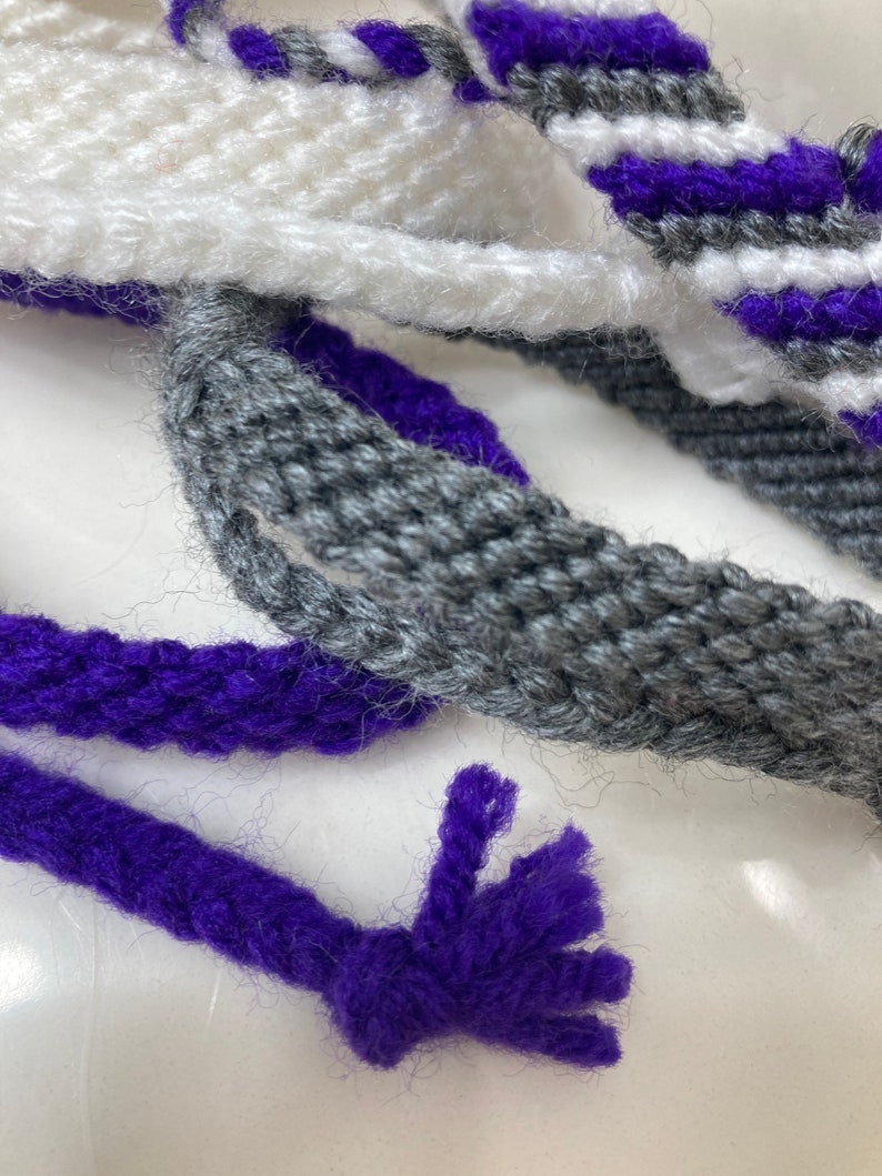 May include: Close-up of three strands of yarn in white, gray, and purple. The purple yarn has a frayed end.