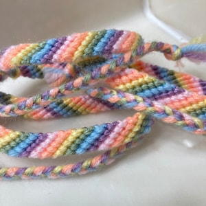 Può includere: Un braccialetto dell'amicizia colorato realizzato con fili intrecciati in tonalità di rosa, blu, verde e giallo.