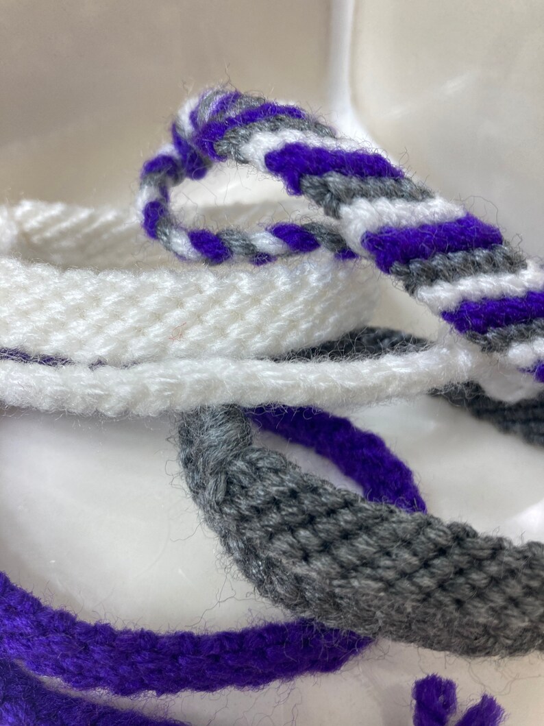 May include: Three braided cords in white, gray, and purple. The cords are woven together in a simple pattern.