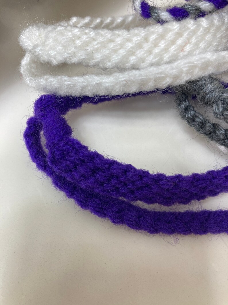 May include: Close-up of three strands of yarn, one white, one purple, and one gray. The yarn is soft and fluffy, and the colors are vibrant.