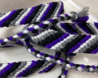 May include: Three friendship bracelets in a black, white, and purple striped pattern.