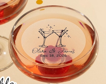 May include: Two clear glass martini glasses with edible cupcake toppers. The toppers are round and feature a black and white illustration of two martini glasses with stars and the text "Olivia & James Dec 18, 2026".