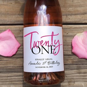 May include: A pink wine bottle with a white label that says "Twenty One" in pink script. The label also says "Finally Legal" and "Amanda's 21st Birthday" with the date "November 16, 2023".