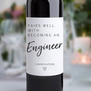 May include: A wine bottle with a white label that reads "PAIRS WELL WITH BECOMING AN Engineer". The label also includes the word "CONGRATULATIONS!" and a heart symbol. The text "The Spirited Labels" and "Personalizable" are at the top.