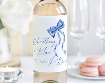 May include: A clear wine bottle with a blue cap and a white label featuring a blue bow and the text "Something Blue Before I Do!". The image also includes two champagne flutes, a candle, and macarons.