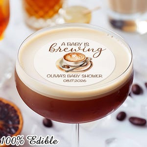 以下が含まれることがあります： ベビーシャワーのドリンクトッパー。茶色と白のコーヒーカップのイラストと「A baby is brewing」と「Olivia's Baby Shower 08.17.2026」のテキストが書かれています。このトッパーは100％食用で、カップケーキのトッピングにも適しています。