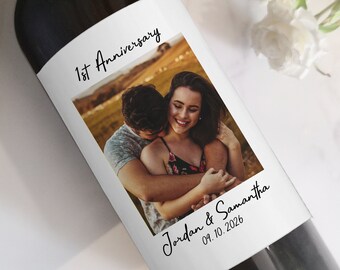 May include: A wine bottle with a custom label featuring a photo of a couple embracing. The label reads "1st Anniversary" at the top, with the names "Jordan & Samantha" and the date "09.10.2026" below the photo. The brand name "The Spirited Labels" is at the top.