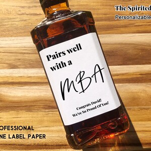 May include: A white label with black text on a brown glass bottle. The label reads "Pairs well with a MBA. Congrats David! We're So Proud Of You!" The Spirited Labels. Personalizable.