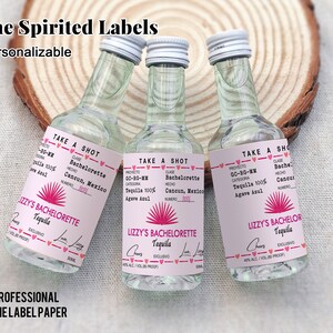 May include: Three small clear glass bottles with pink and white labels. The labels feature a pink sunburst design and the text "Lizzy's Bachelorette Tequila" and "Lizzy's Bachelor Tequila".