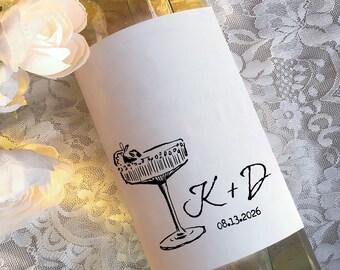 May include: White wine bottle with a personalized label featuring a black and white illustration of a cocktail glass and the text "K+D 08.13.2026".