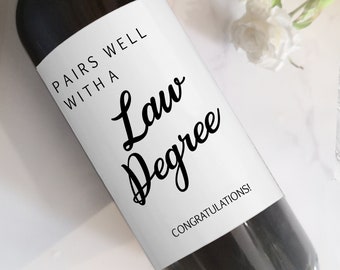 May include: A wine bottle with a white label that reads "PAIRS WELL WITH A Law Degree" in black script. The word "CONGRATULATIONS!" is printed at the bottom of the label. The top of the bottle has the text "The Spirited Labels".