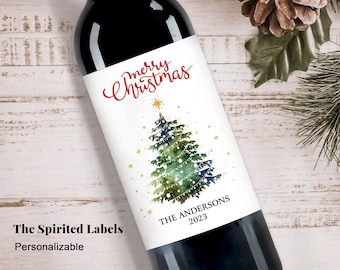 May include: A wine bottle with a personalized Christmas label. The label features a watercolor Christmas tree with gold stars and the words "merry Christmas" in red script. The family name and year are also printed on the label.