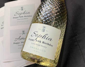 Può includere: Una bottiglia di Prosecco in vetro trasparente con un'etichetta bianca. L'etichetta ha un testo nero che recita "Sophia Happy 40th Birthday Love from Henry Prosecco DOC".