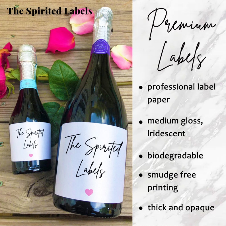 May include: Two bottles of sparkling wine with labels that say "The Spirited Labels". The labels are white with black text and a pink heart. The bottles are on a wooden surface with rose petals.